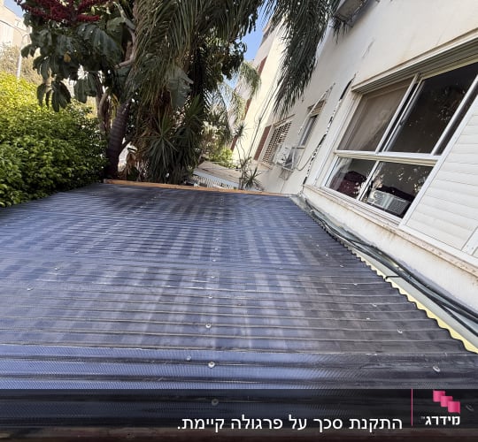 התקנת סוכך קבוע מלוחות גליים כהים בצמוד לקיר בית